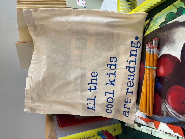 Canvas tote bag with blue writing, "All the cool kids are reading"