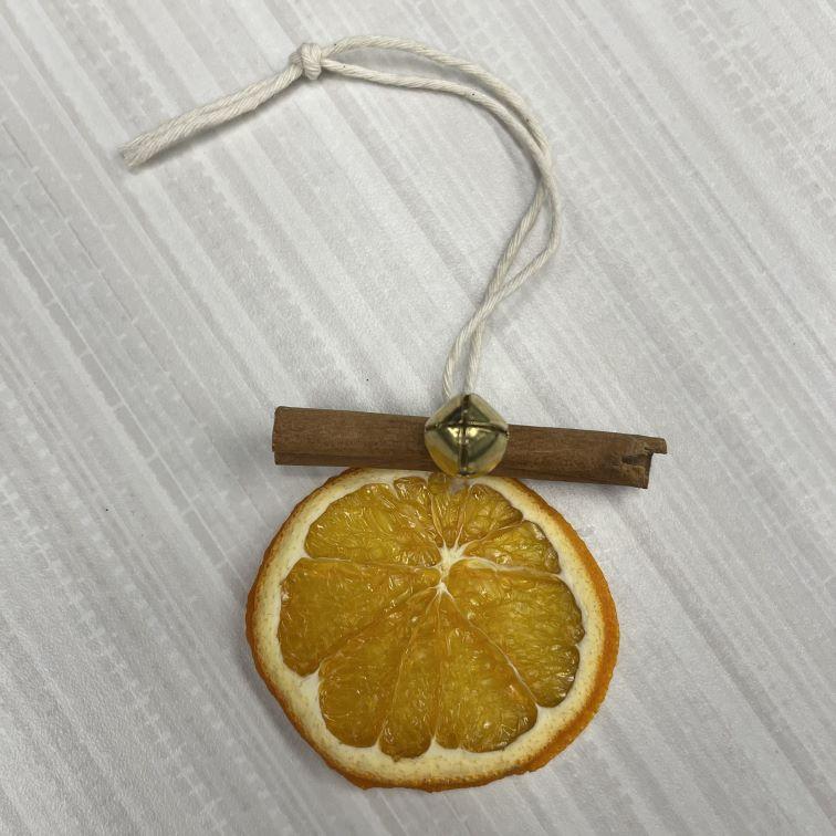 Dried orange slice on a string with a cinnamon stick and jingle bell